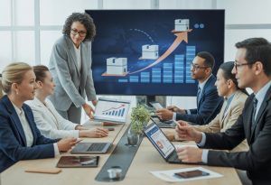 Business professionals in a meeting room discussing delivery plans with charts and digital maps displayed.
